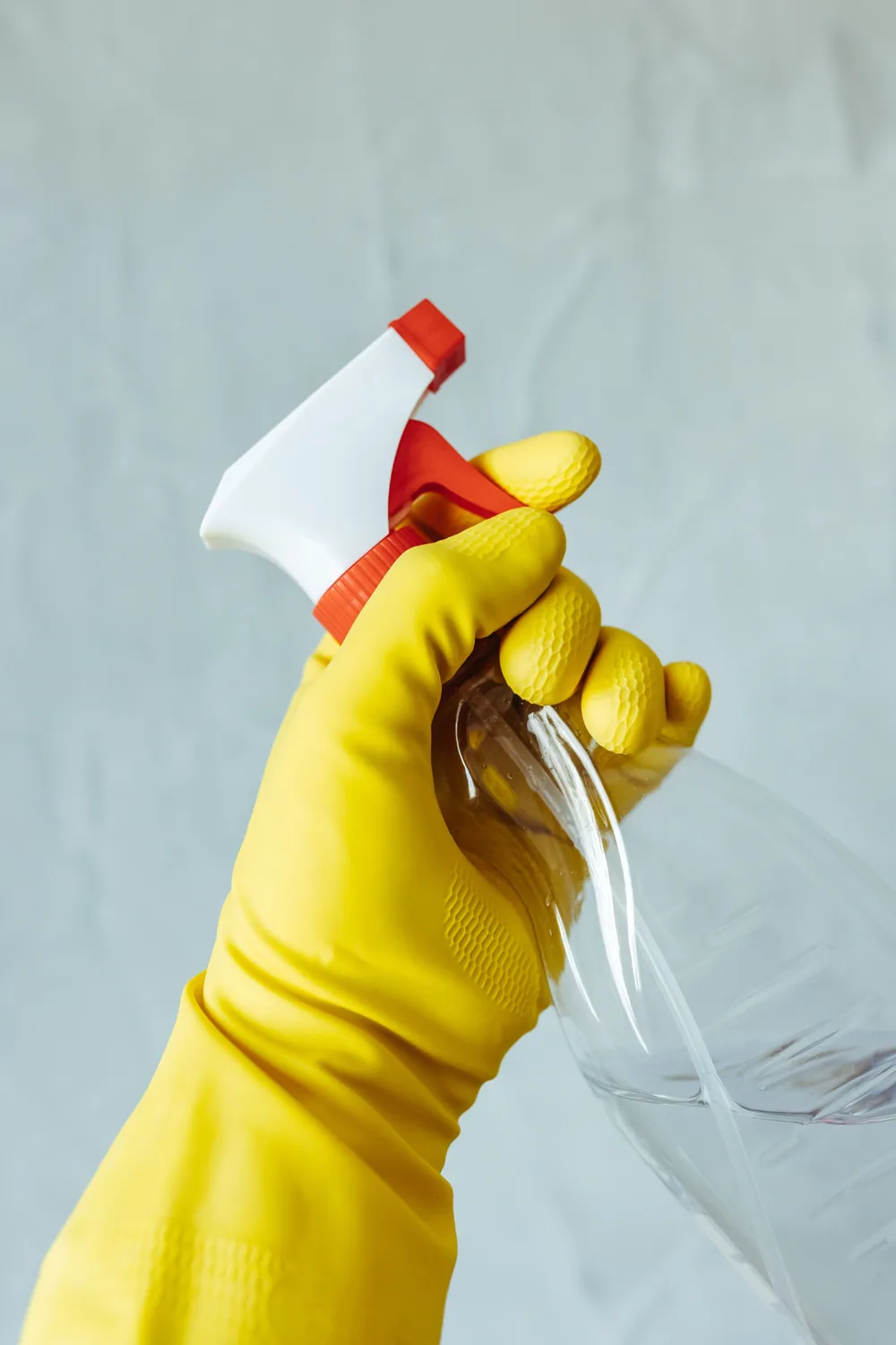 Gloved hand holding a spray bottle of cleaning solution